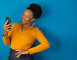 © Patricia Fragoso - black woman smiling and  holding a cellphone on studio with a blue blackground