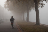 Fototapeta  - People cycling or waking outdoors during a very foggy, misty day