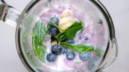 Wall Mural - Blueberry, banana and spinach smoothie or milkshake blended in blender with splashes. top view. slow motion. Healthy drink concept
