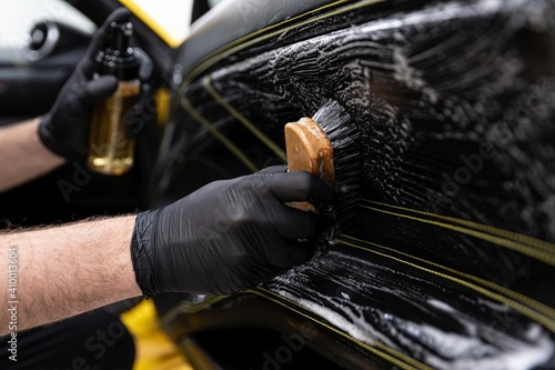 Car wash worker cleaning an brushing car leather upholstery. Modern car interior