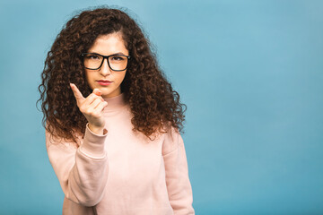 Attention, listen to me! Close up portrait of young curly woman wagging her finger isolated over blue background. Negative human emotions facial expression.