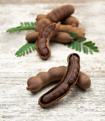 Wall Mural - Tamarind fruits with green leaves on wood background.