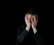 © tab62 - Depressed man with face down in both hands while surrounded by darkness