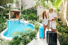 Happy Young Asian Couple With Suitcases Standing At Swimming Pool With Suitcases And Looking At Each Other