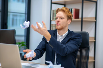 Young man juggling with crumpled paper in office