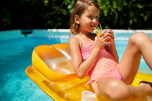 Little Girl Relaxing In Swimming Pool, Enjoying Suntans, Drink A Juice On Inflatable Yellow Mattress