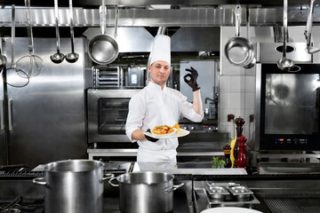 Chef in the restaurant holds a plate with a ready-made dish and shows the 