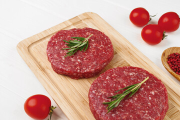 Two raw beef burger patties on wooden board