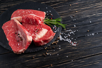 Wall Mural - Three pieces of juicy raw beef on a stone cutting board on a black wooden table background.