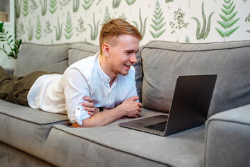 Handsome young relaxing man using laptop and lying on the sofa