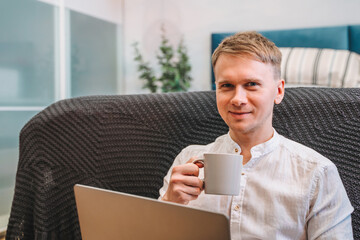 Canvas Print - attractive man drinking coffee while working on his laptop in bedroom. working from home in quaranti
