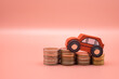 Red toy car on pile money stack coins growth on pink background. Miniature automobile model and business finance statement vehicle buy, loan, rent. Transportation insurance auto care industry concept.