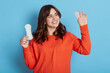 © sementsova321 - Cheerful magnetic cute dark haired woman holding menstrual cup and sanitary pad in both hands, looking hygiene product with smile, find suitable solution for period, wearing orange sweater.