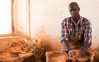 Skilled african american potter working on potters wheel making clay products in pottery workshop