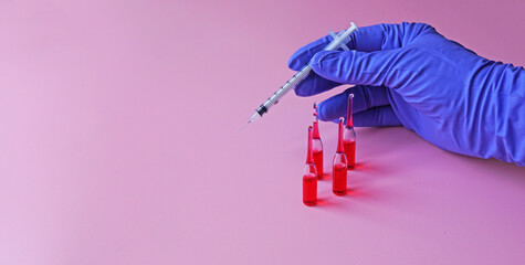 Ampoules with red liquid on the background of a hand in a blue glove holding a syringe  