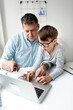© epiximages - Father and son sitting in front of the laptop, working from home with help from his son.