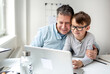 © epiximages - Father and son sitting in front of the laptop, working from home with help from his son.