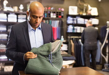 Confident young adult man looking for pullover in mens clothing boutique