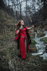 Red-haired woman in a red dress in a historical Celtic costume in the autumn forest