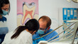 © DC Studio - Close up view of pediatric dentist and assistant cleaning tooth for little girl in dental clinic sitting in stomatological chair. Doctor and nurse working in dental clinic using sterilized tools.