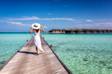 Wall Mural - back view of a elegant woman in white dress and hat walks down a pier over turquoise ocean in the ma