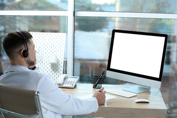 Doctor with headset consulting patient online at desk in clinic, space for text. Health service hotline