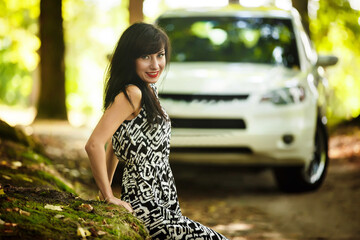 beautiful brunette in a dress posing in nature near a white car