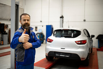 Portrait of professional car mechanic standing in vehicle workshop with thumbs up.