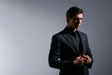 Portrait of handsome young man in black stylish suit, over on dark grey background. Space for text.