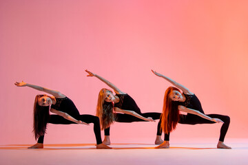 Wall Mural - group of three ballet girls in black tight-fitting suits dancing on red background with their long hair down.