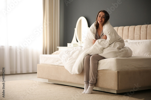 Beautiful young woman wrapped with soft blanket sitting on bed at home © New Africa