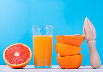 Blood orange juice freshly squeezed in the drinking glass with pulp, wooden juicer and the fruit peels against the blue colorful background