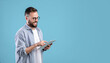 © Prostock-studio - Smart millennial guy in glasses using tablet computer over blue studio background, banner design with copy space