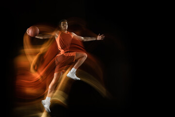 Carry on winning. Young arabian muscular basketball player in action, motion on black background in mixed light. Concept of sport, movement, energy and dynamic, healthy lifestyle. Training, practicing