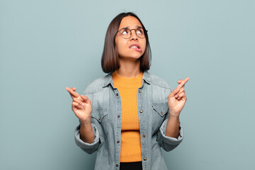 Wall Mural - young hispanic woman crossing fingers anxiously and hoping for good luck with a worried look