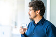 © Joao - Casual businessman holding and drinking glass of water. Healthy man at home office portrait looking throught the window