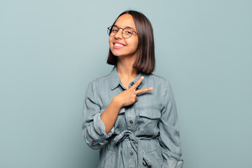 Canvas Print - young hispanic woman feeling happy, positive and successful, with hand making v shape over chest, showing victory or peace