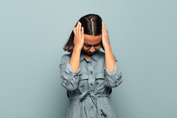 Wall Mural - young hispanic woman feeling stressed and frustrated, raising hands to head, feeling tired, unhappy and with migraine