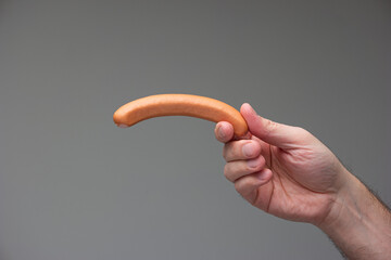 Caucasian male hand holding a bratwurst dog between fingers isolated on gray background