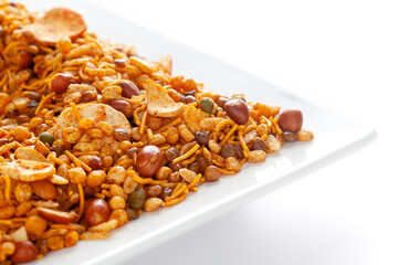 Wall Mural - Hot spicy NavRatan snacks in a white ceramic square plate, made with red chili, peanuts, corn flakes, etc. Pile of Indian spicy snacks (Namkeen), under backlight, side view