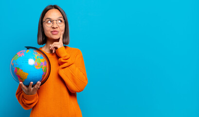 young hispanic woman smiling happily and daydreaming or doubting, looking to the side