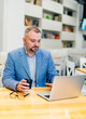 © Vadim - Businessman sitting at table in a cafe and working. Handsome middle aged man in blue suit with cup of coffee.