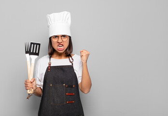 Sticker - young hispanic woman shouting aggressively with an angry expression or with fists clenched celebrating success