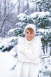 © petrrgoskov - Outdoor winter portrait of happy smiling woman posing in park in front of fir tree. Model wearing warm white sweater.