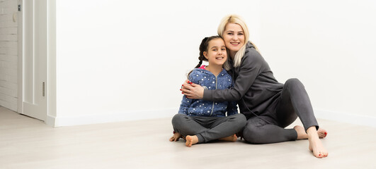 Wall Mural - young mother and little daughter near white wall and hugging