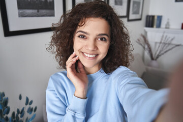 happy pretty hispanic gen z teen girl holding smartphone looking at camera taking selfie shot for so