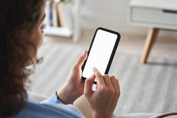 Young woman or teen girl hands holding cell phone touching finger mockup white blank display, empty screen for social media app ad at home. Mobile application tech concept, over shoulder closeup view.