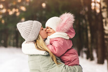 Young Mother In Winter Holds Her Little Daughter In Her Arms And Kisses Her. Family Portrait. Motherhood And Childhood