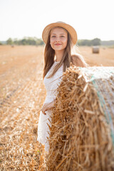 Poster - Smiling girl in a white dress and a straw hat in the agricultural field. Rural portrait of a beautiful girl