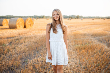 Canvas Print - Young girl in a white dress in the field of harvested rye. Portrait of a cheerful girl in the field